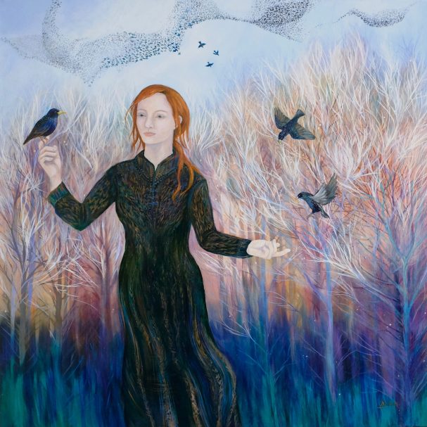 A woman in a black dress stands among trees, releasing birds into the sky.